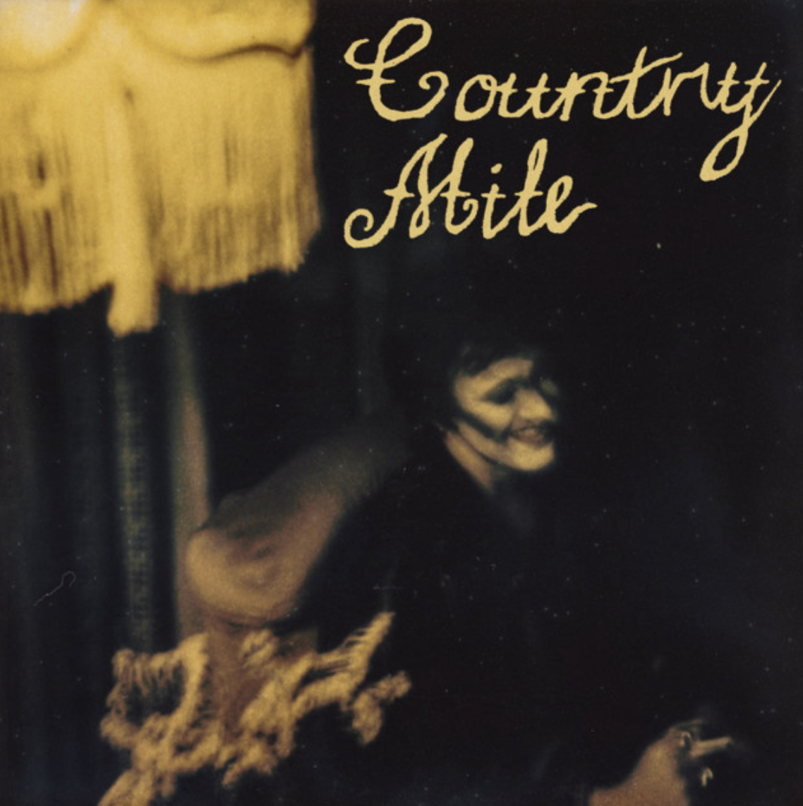 Album cover artwork for Country Mile by The Grogans, featuring cursive text beside a vintage dim-lit scene.